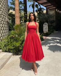 Woman in a red dress standing outdoors with palm trees and a building in the background