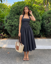Woman in a black dress holding a straw bag in a garden setting